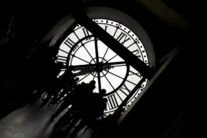 Schwarz-Weiss Bild einer riesigen Uhr, davor die Silhouetten einer Gruppe von Menschen